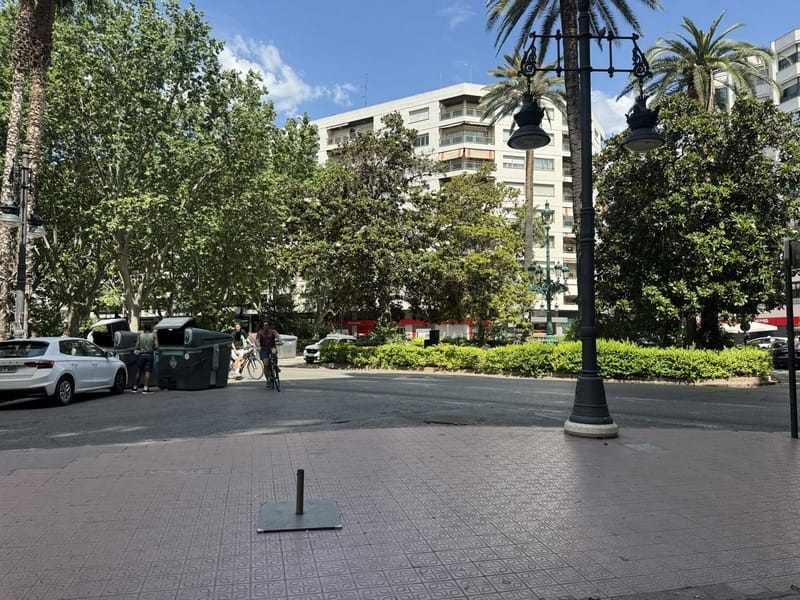 Fotografía de campo: calle arbolada con edificios de viviendas en bloque, farolas y aceras amplias.